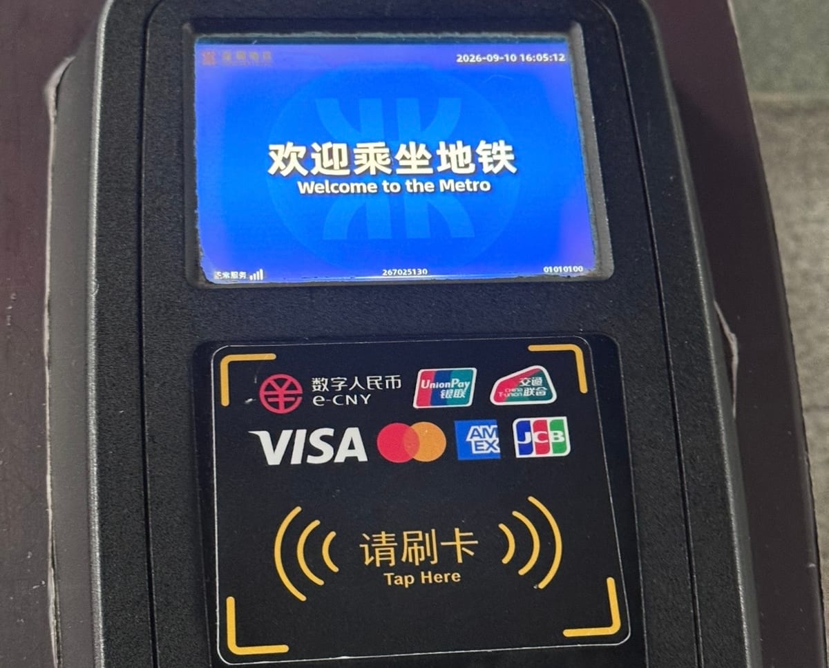 The international card reader on a Shenzhen Metro gate: Visa, Mastercard, American Express and JCB logos above "请刷卡 / Tap Here". Photographed September 2026.